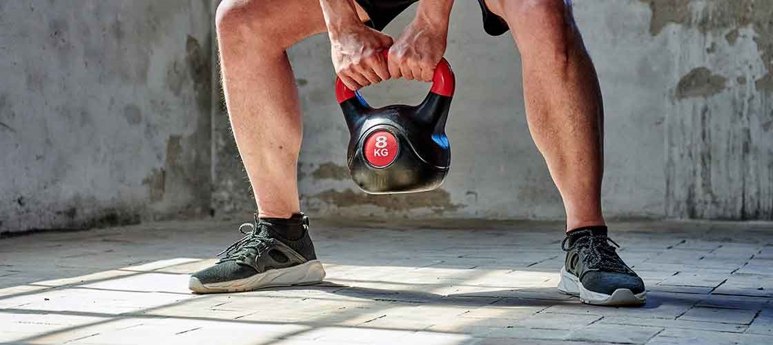 En person utfører en knebøy med en 8 kg kettlebell på et lyst treningsgulv.
