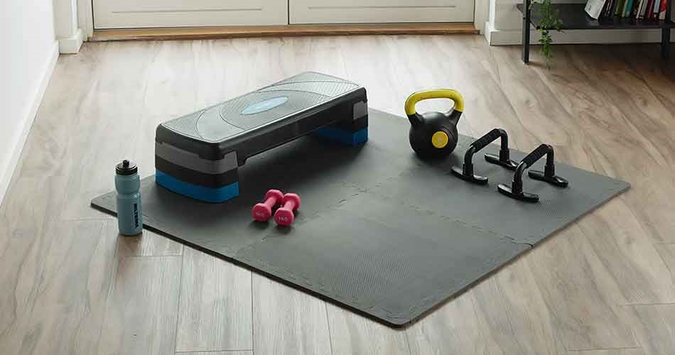 En treningsmatte med stepkasse, kettlebell, manualer, push-up-håndtak og drikkeflaske er klar til hjemmetrening.
