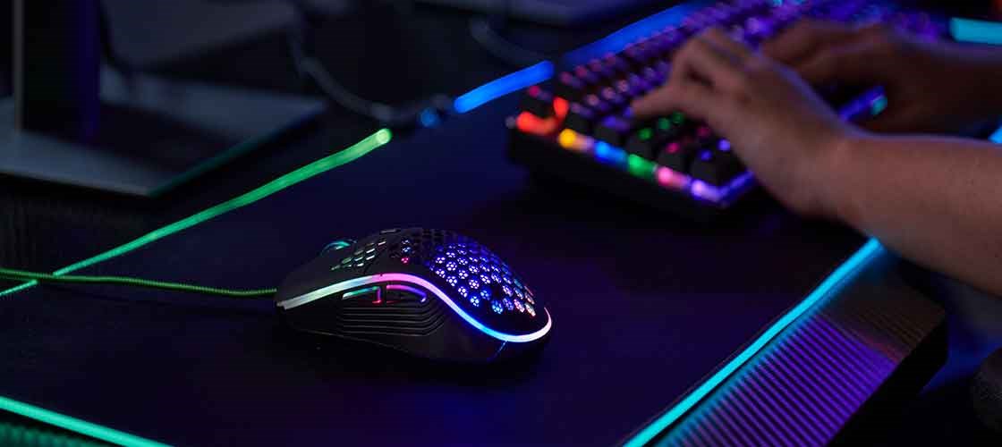 Gamingmus med RGB-belysning på et skrivebord ved siden av et opplyst gamingtastatur.