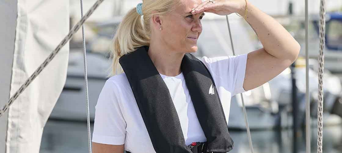 Kvinne som står på dekket til et seilskip iført en oppblåsbar redningsvest. Brukt som inspirasjon for guiden: «Slik sjekker du den oppblåsbare redningsvesten din – trinn for trinn».