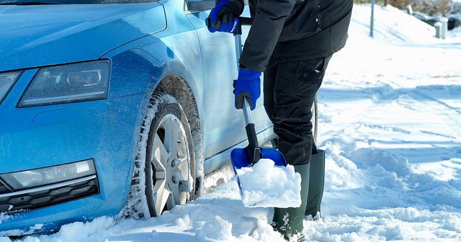 Person removing snow around a car wheel with a Biltema snow shovel.