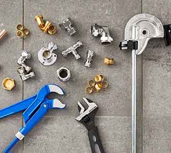 A close-up of various plumbing fittings and plumbing tools scattered on a gray stone floor.
